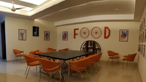 A conference room with a large table surrounded by orange chairs, a ceiling fan, and artwork on the walls. - PLLAZIO Residency (Gurugram)