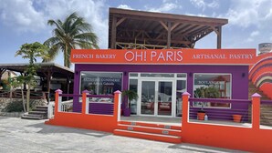 A French bakery named "OH! PARIS ARTISANAL PASTRY" with a purple and orange facade, featuring a storefront with glass doors and steps leading up to the entrance.