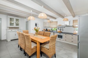 Enjoy meals in the kitchen with a central island and dining area, featuring a refrigerator, various appliances, and a wooden table with wicker chairs.