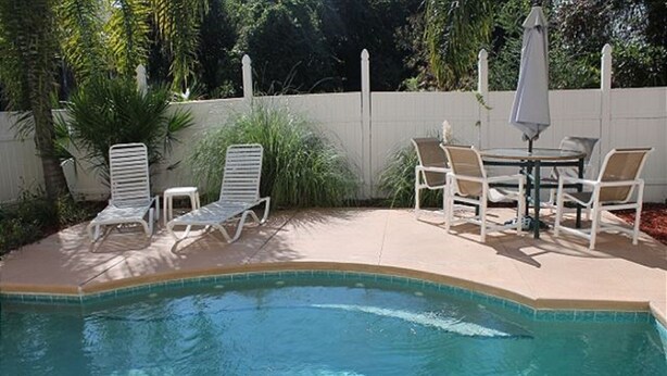Une piscine à l’eau d’un bleu cristallin, entourée de chaises longues blanches et d’une table avec des chaises.