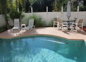 A pool with clear blue water, surrounded by white lounge chairs and a table with chairs.