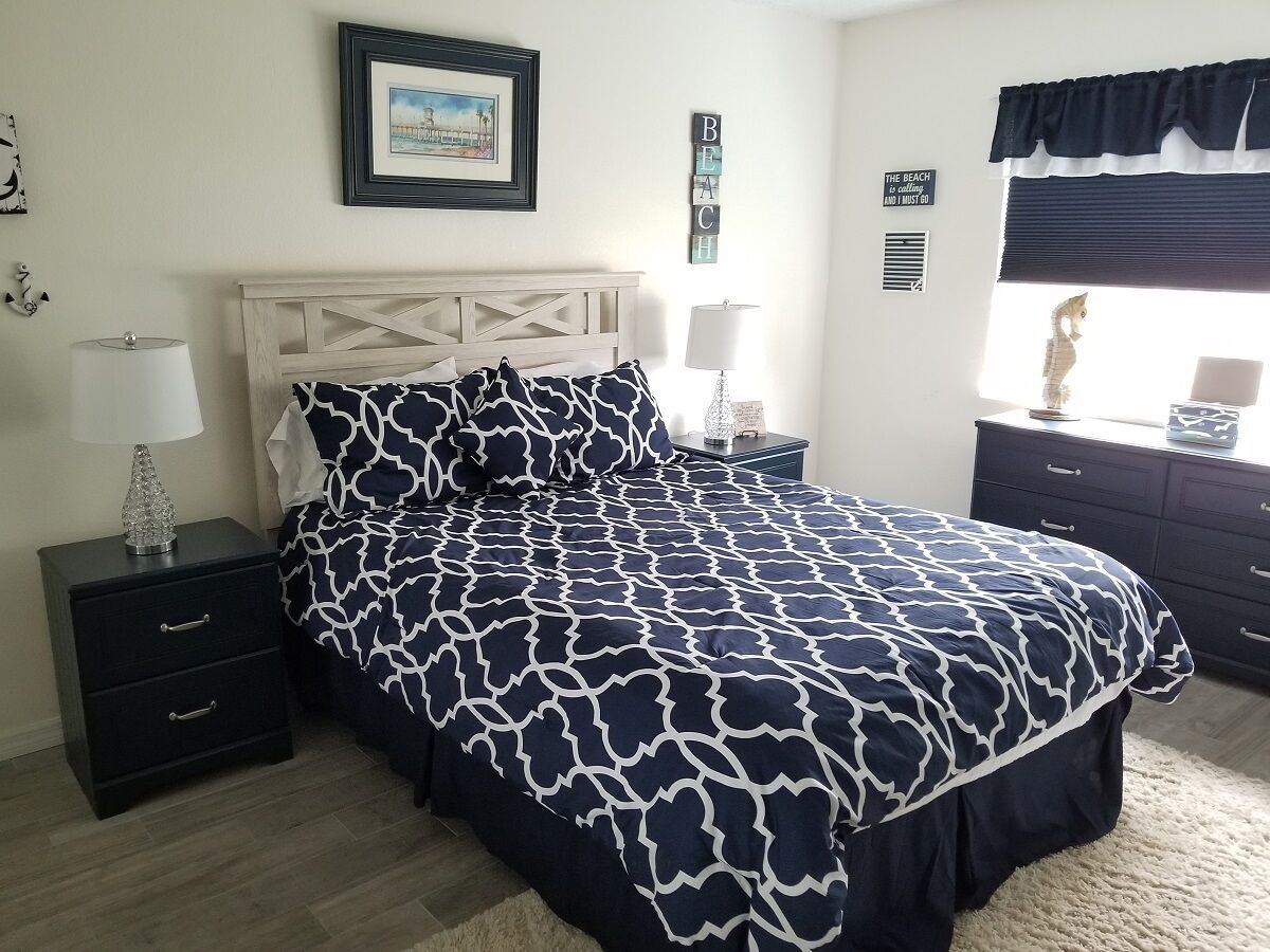 A bedroom with a bed, two bedside tables, a nightstand, a dresser, a window with a view, and a framed picture on the wall.