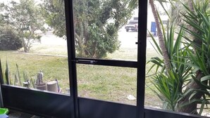 Una habitación con puerta corredera de vidrio que da a un espacio exterior con césped, árboles y un vehículo estacionado.