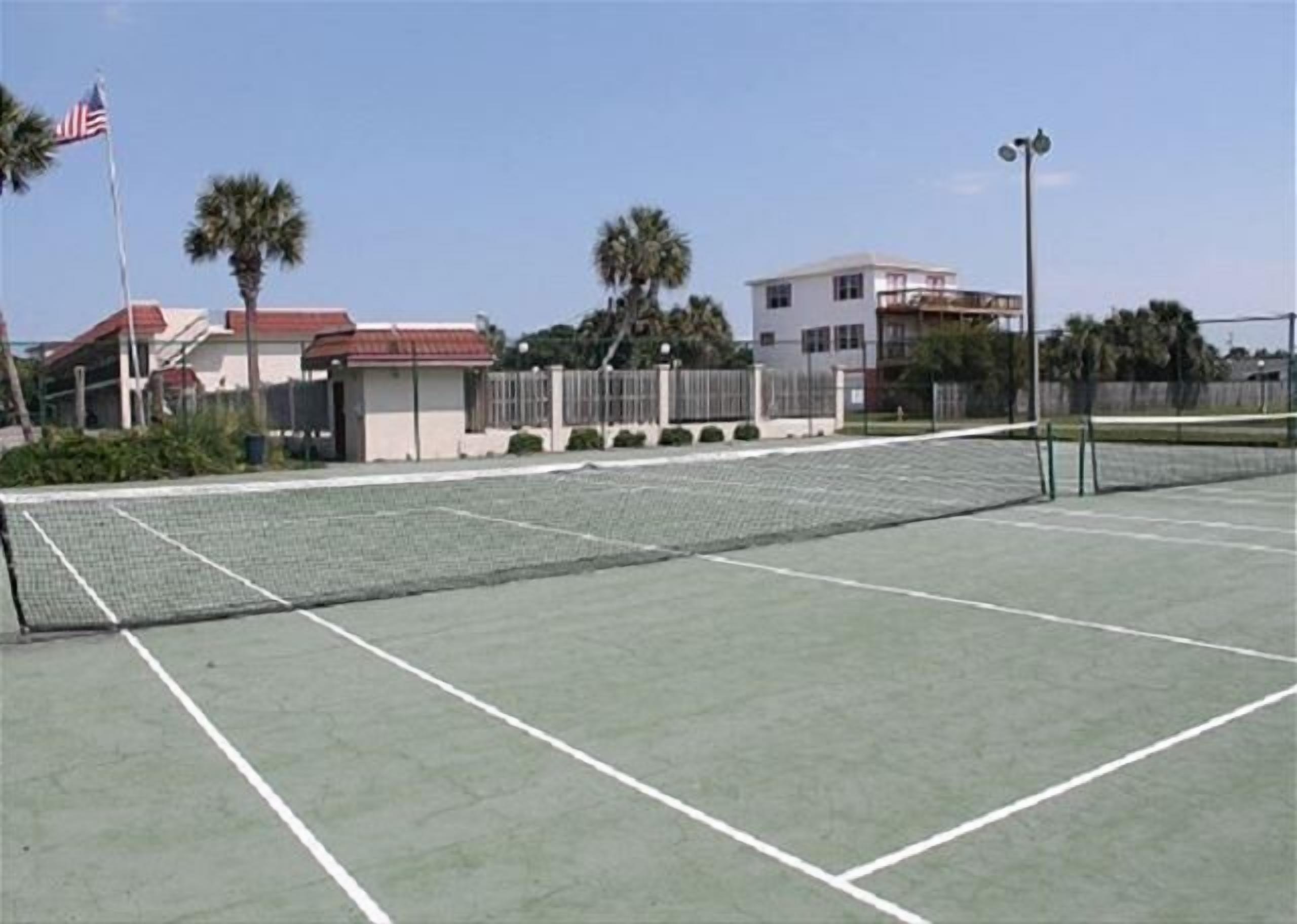 Ein Tennisplatz im Freien mit Netz, umgeben von einer Umzäunung und Palmen.