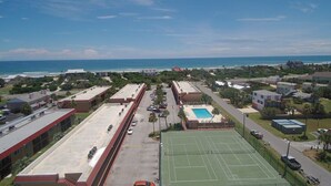 Ett flygbildsfoto av ett område vid kusten med en tennisbana, en pool och byggnader.