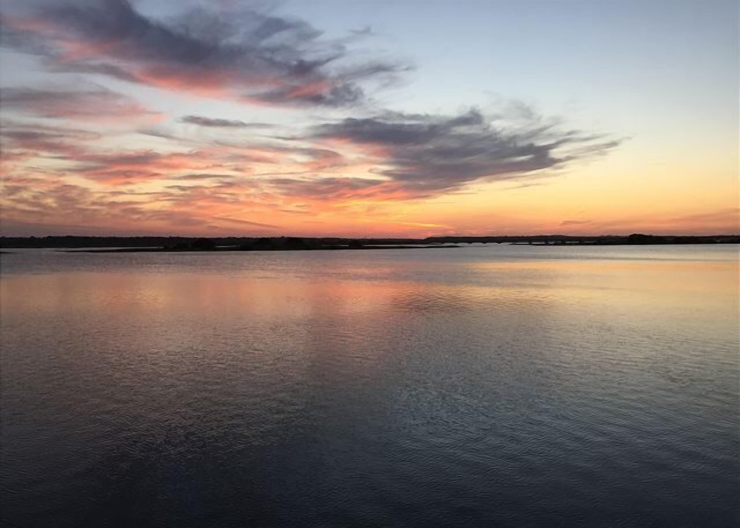 Un cuerpo de agua tranquila reflejando el cielo durante el atardecer.