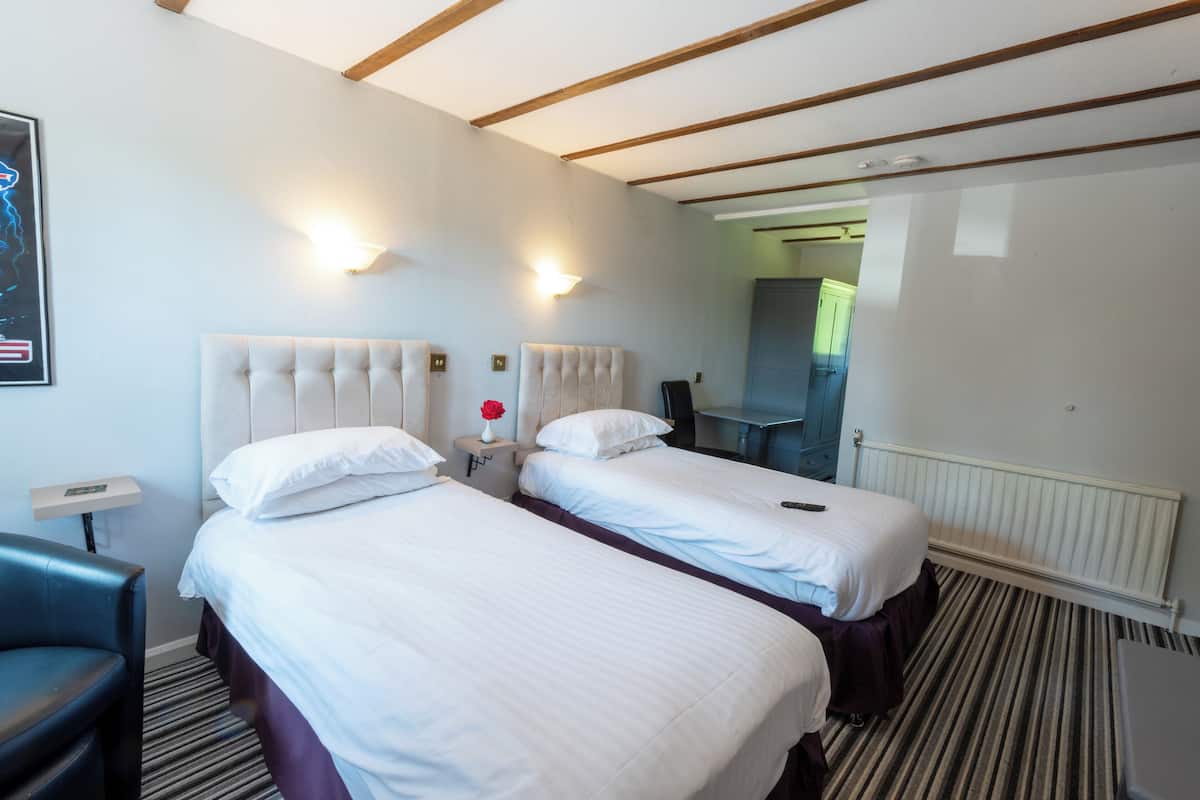 A hotel room with two beds, a desk, a chair, and a radiator.