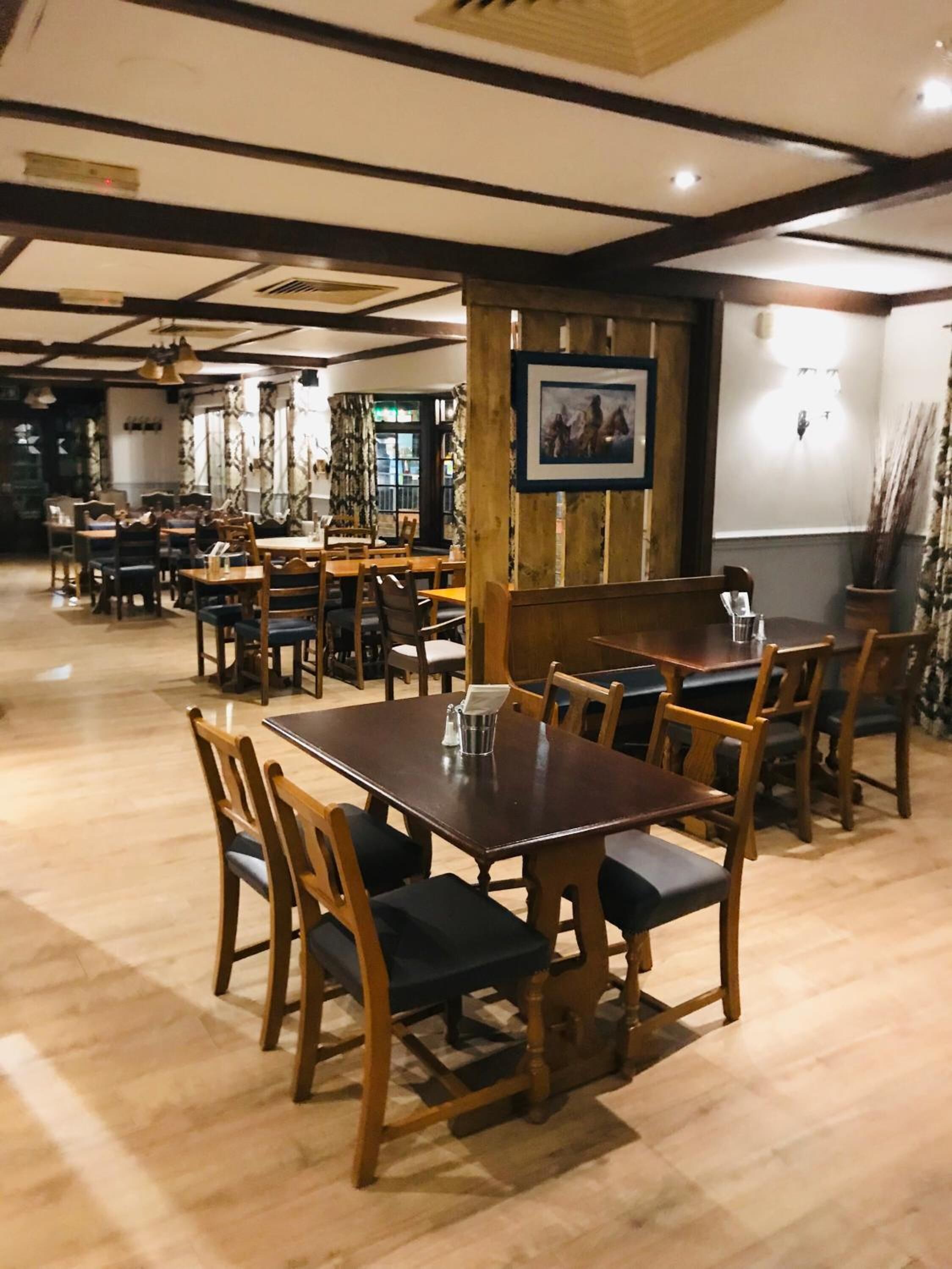 Ein Restaurant mit Holztischen und -stühlen, einer Holzsäule mit einem gerahmten Bild und einer Holzwand mit freiliegenden Balken.