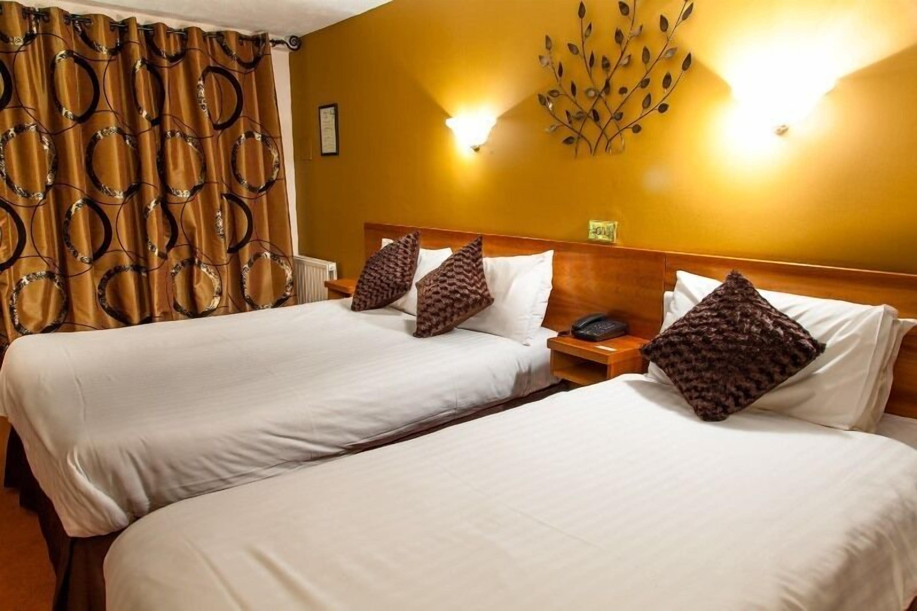 A hotel room with two beds, a wooden headboard, a decorative wall piece, and a curtain with a circular pattern.