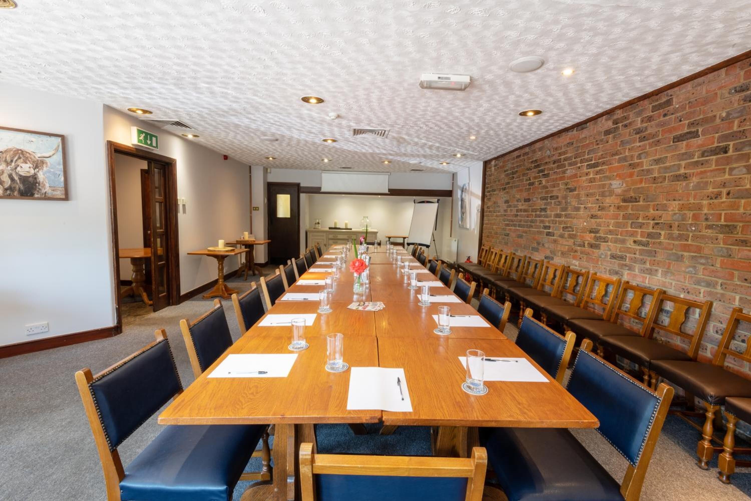 A conference room with a long wooden table, blue chairs, and a brick wall.