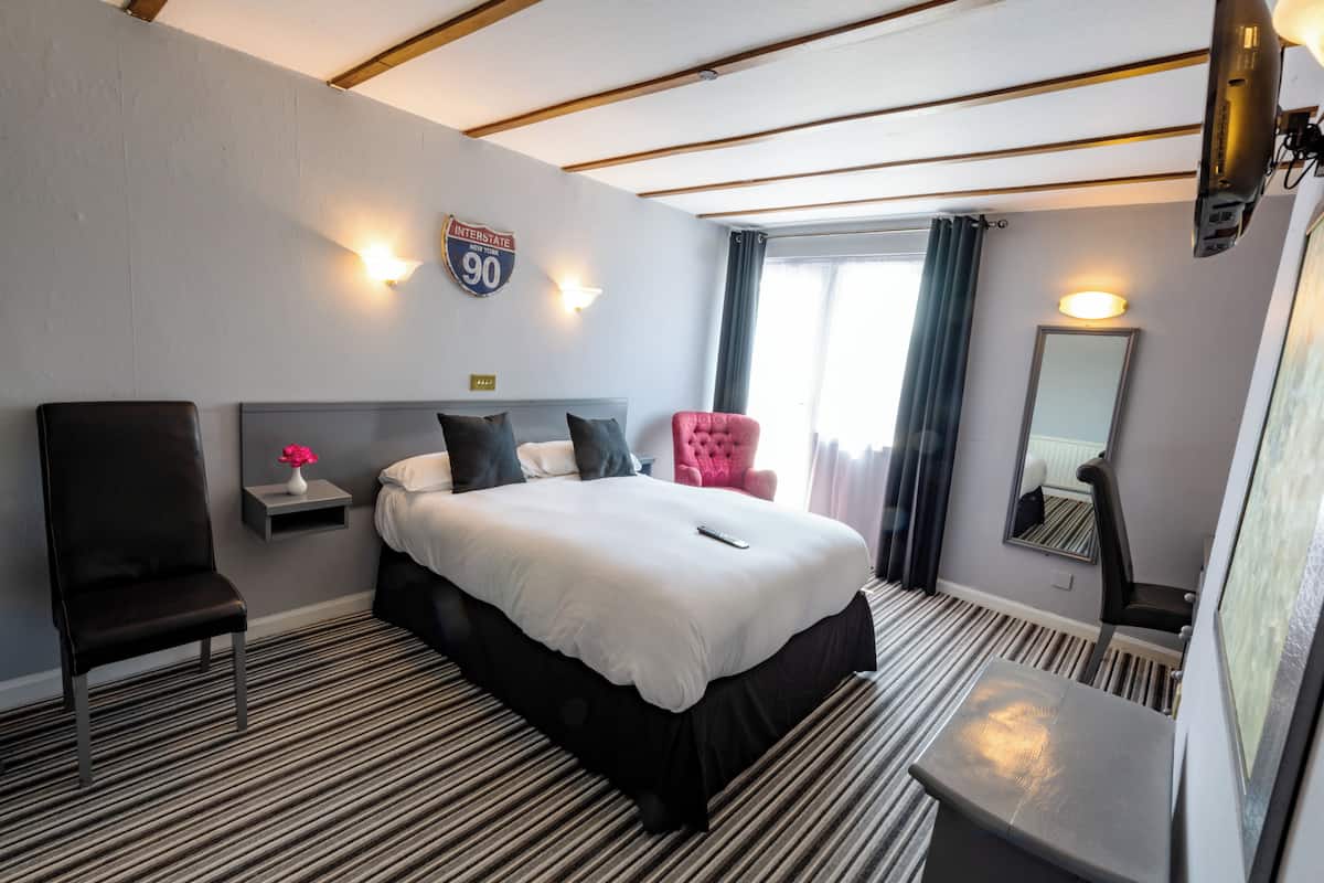 A hotel room with a bed, a chair, a nightstand, a mirror, and a window with curtains.