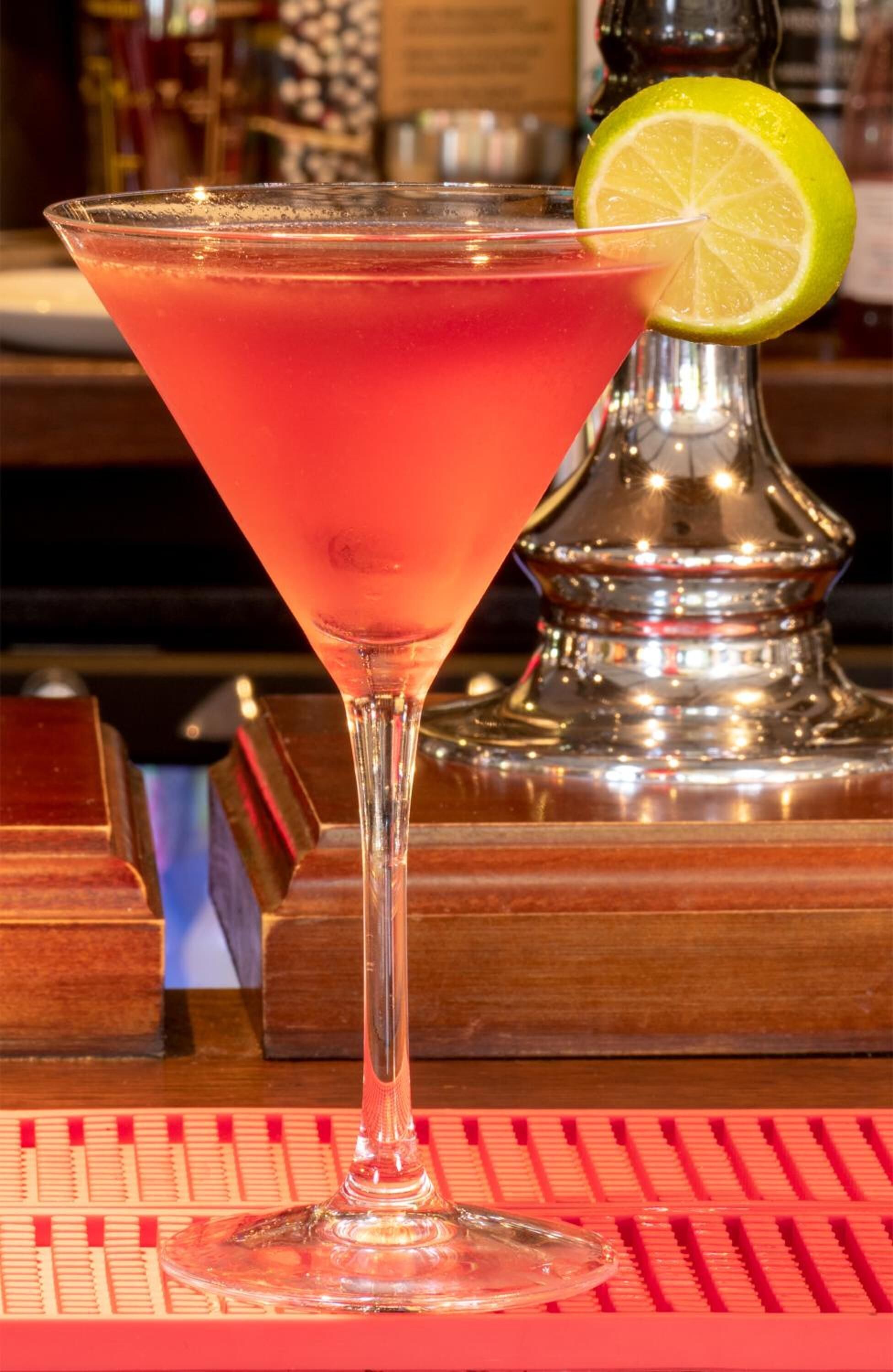 A cocktail in a martini glass with a lime garnish on a bar counter.