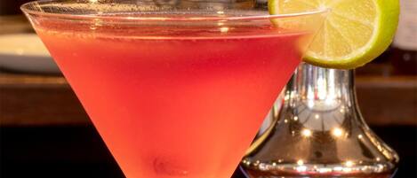 A cocktail in a martini glass with a lime garnish on a bar counter.