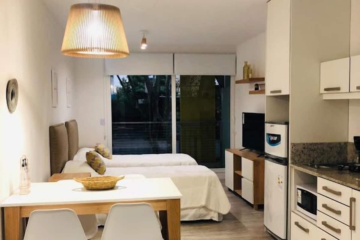 A compact hotel room with a dining area, a bed, and a kitchenette.