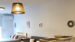 Una habitación moderna y luminosa con una cama, un sofá gris, un escritorio de madera con dos sillas y una lámpara colgante.
