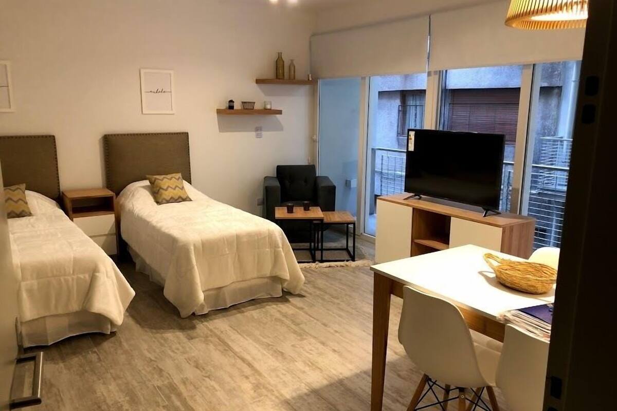 A hotel room with two beds, a desk with a chair, a television, and a window with a view of the outside.
