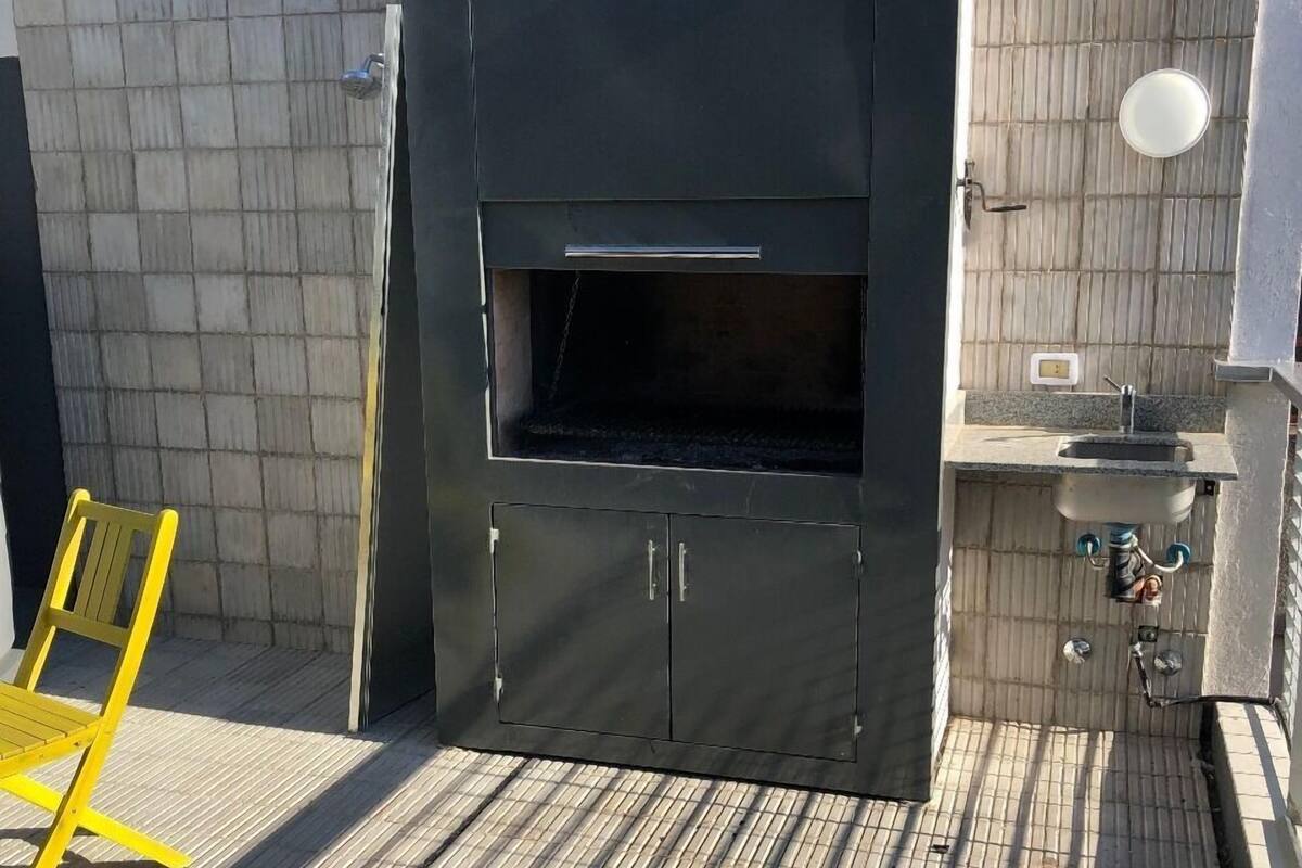 A barbecue area with a built-in grill, a sink, and a yellow chair.