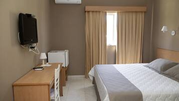 Una habitación de hotel con cama, escritorio, computadora, televisor y aire acondicionado.