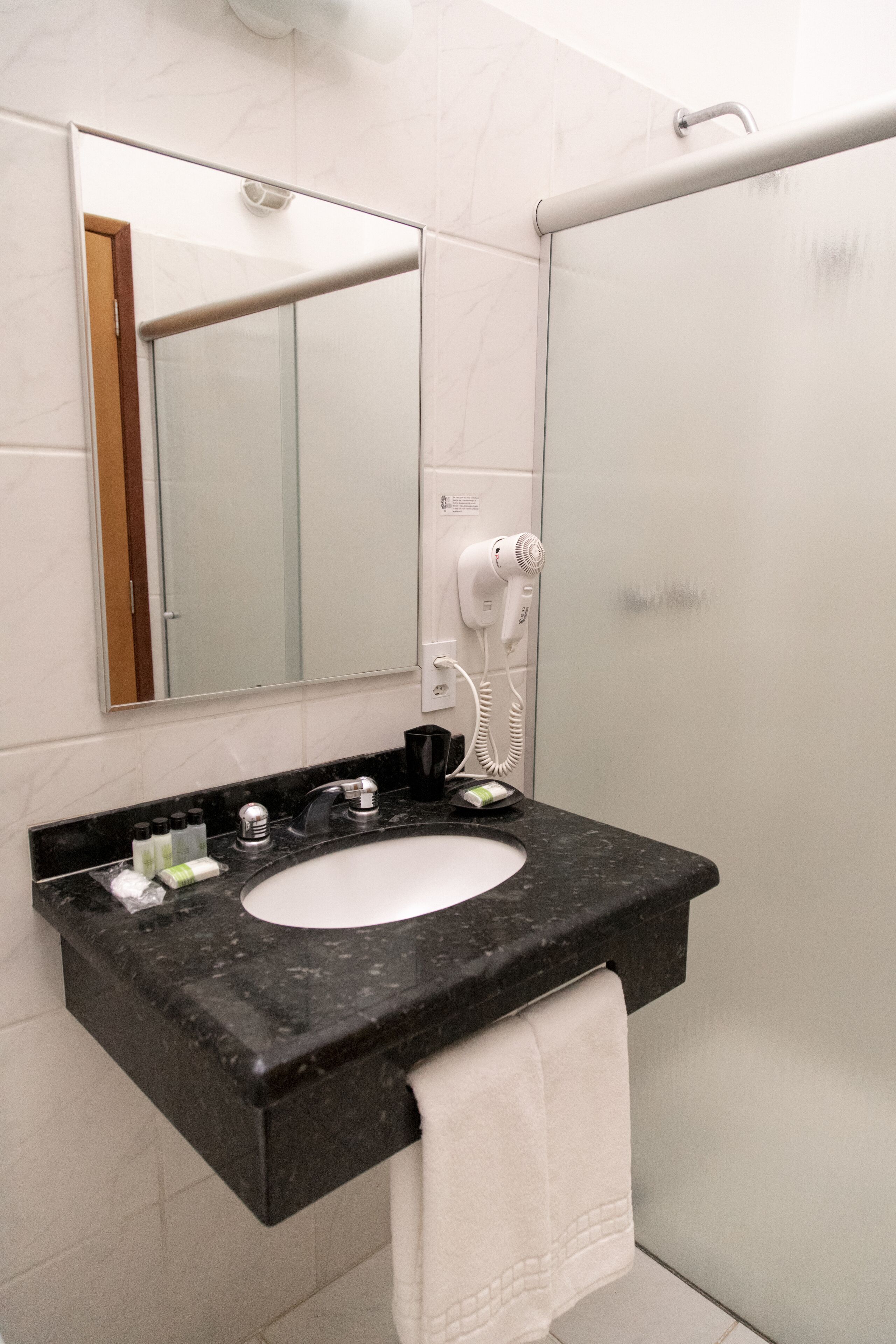 A bathroom with a black marble sink, a mirror, a hairdryer, and a towel hanging on the wall.