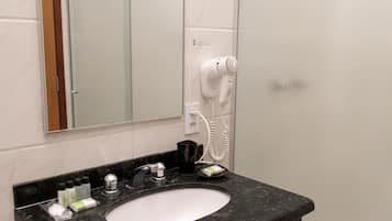 A bathroom with a black marble sink, a mirror, a hairdryer, and a towel hanging on the wall.