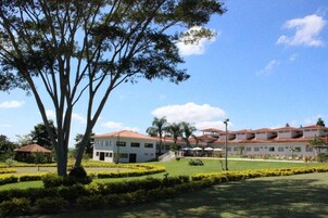Um hotel com vários edifícios brancos, um gramado bem cuidado e uma grande árvore em primeiro plano.