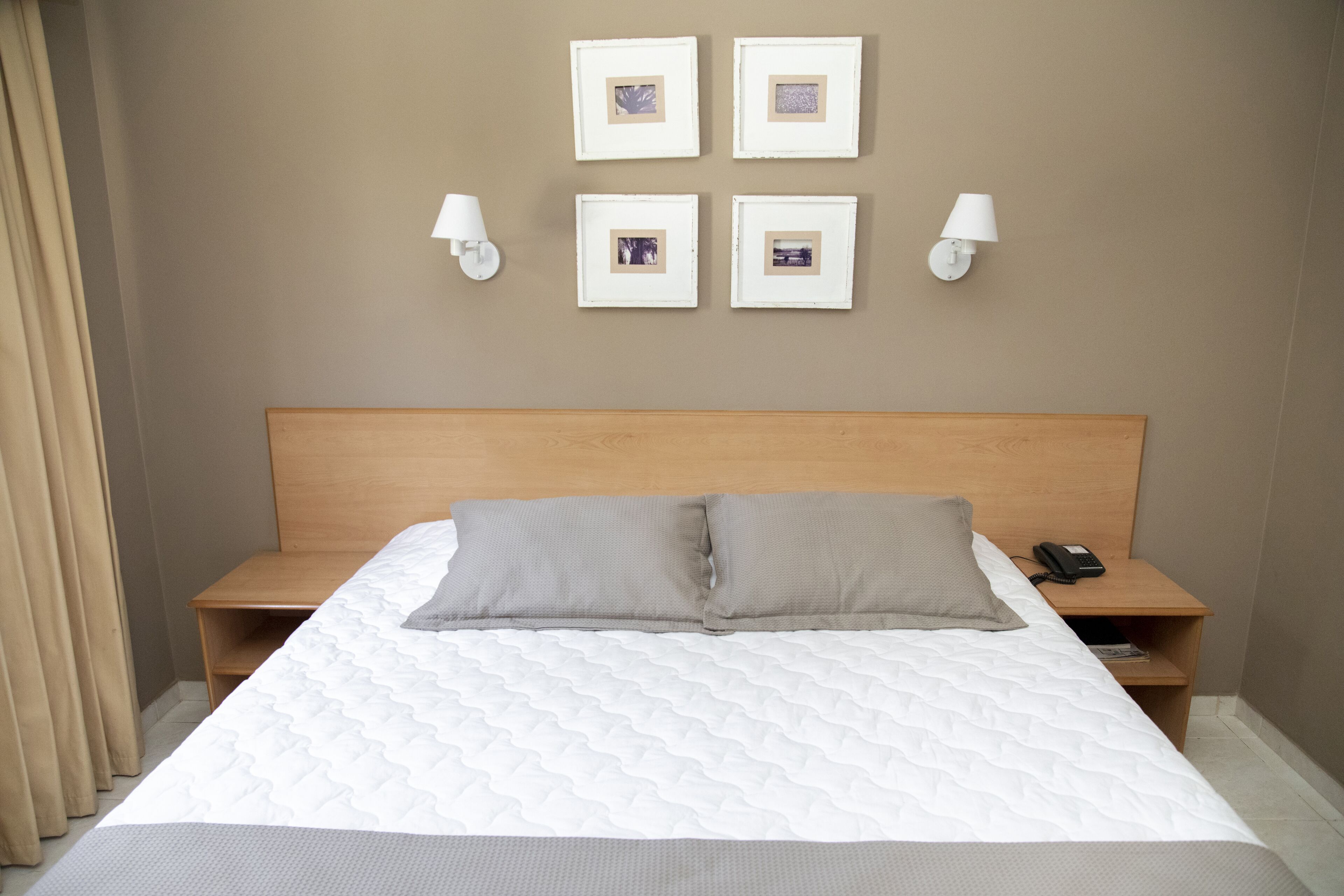 Una cama bien hecha con cabecera de madera, dos mesitas de noche con lámparas y cuatro cuadros enmarcados en la pared.