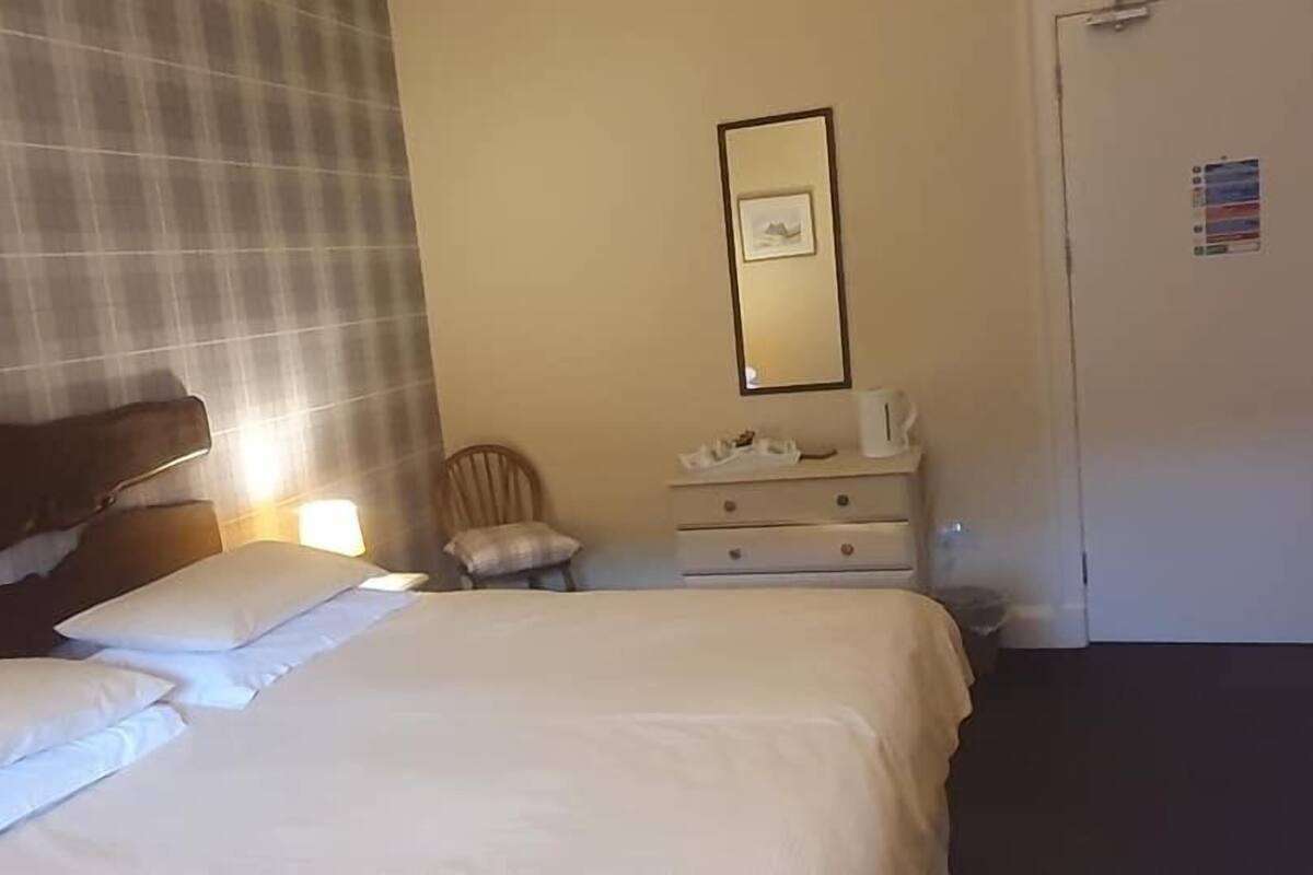A hotel room with a bed, a chair, a dresser, and a door.