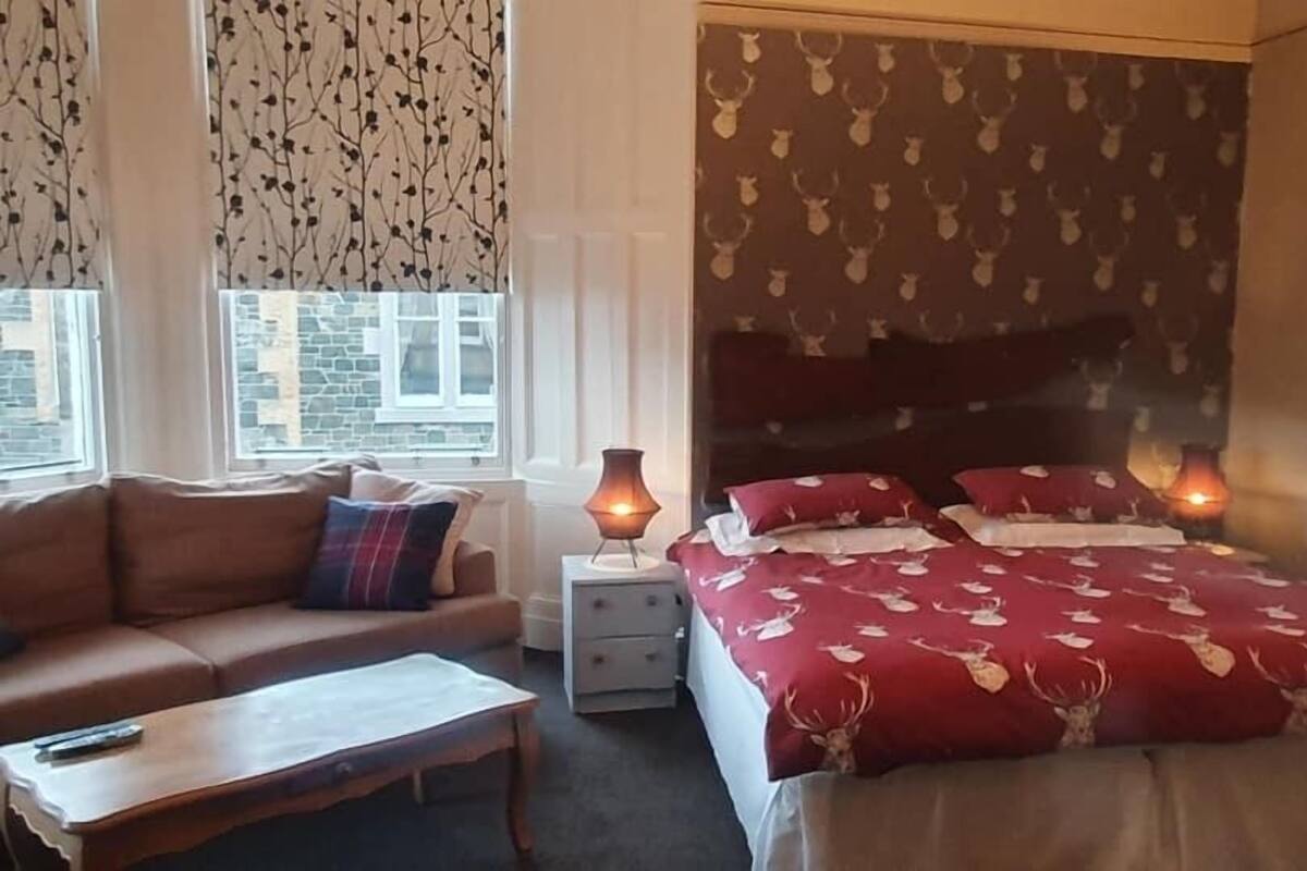 A bedroom with a bed, a nightstand, a bedside table, a sofa, and a window with curtains.