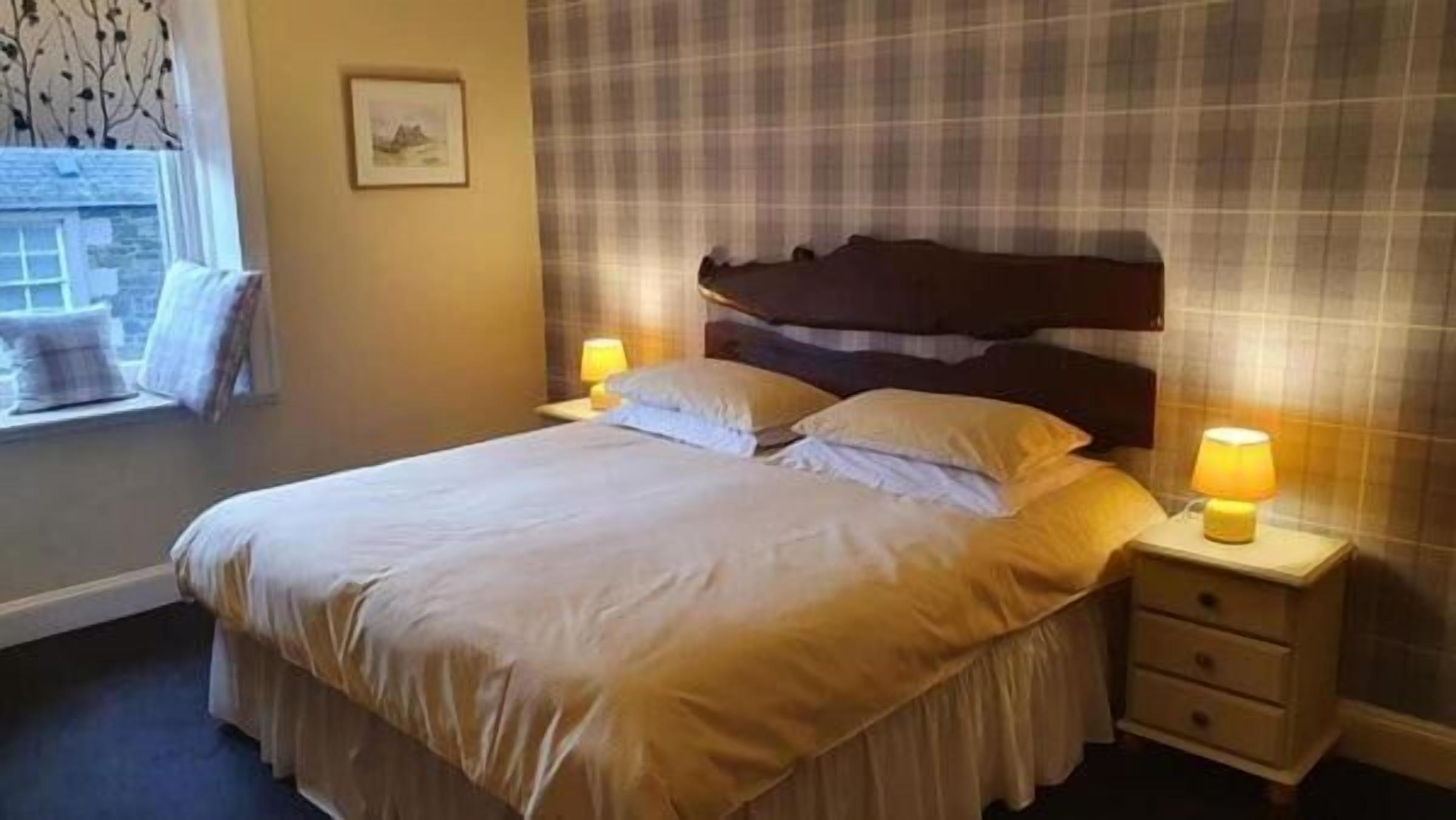 A neatly made bed with a wooden headboard, two bedside tables with lamps, and a window with a view of trees.