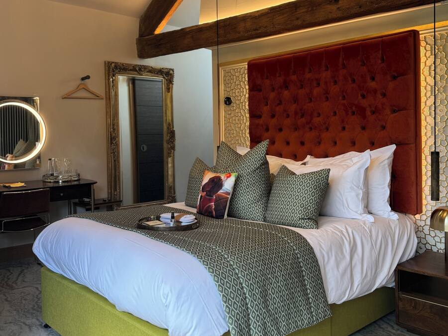 Una cama grande con base tapizada en verde, cabecera capitonada roja y ropa de cama estampada.