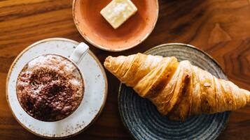 Un croissant en un plato, una taza de café y un bol pequeño con un trozo de mantequilla.