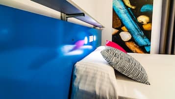 Habitació d'hotel amb un llit, una paret blava, una finestra que dona a unes roques i un almoiner vermell.