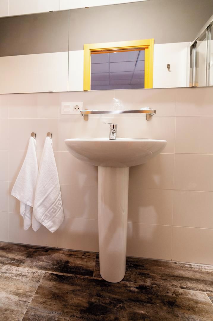 A bathroom with a pedestal sink, a towel rack with two towels, and a window with a yellow frame.