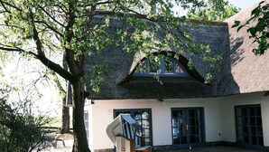 Un bâtiment traditionnel avec un toit de chaume, de grandes fenêtres et une chaise en bois dotée d’un coussin à rayures.