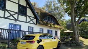 Une voiture jaune est garée devant un bâtiment traditionnel doté d’un toit de chaume et d’un mur en pierre.
