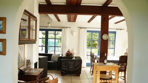 Un salon chaleureux avec un canapé, une table en bois et des chaises. Il y a une fenêtre avec des rideaux et une horloge au mur.