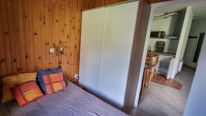 Ein Schlafzimmer mit hölzernem Kopfteil, einem Bett mit bunten Kissen, einem Nachttisch und einem Kleiderschrank.