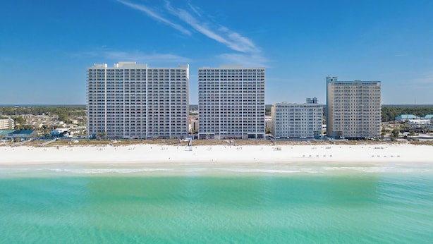 Un hotel frente a la playa con varios edificios altos, una playa de arena y aguas turquesas cristalinas.