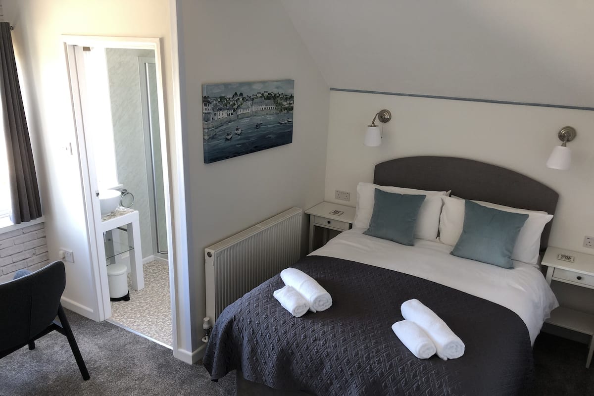 Ett hotellrum med en säng, ett skrivbord, en stol, ett litet bord, ett element och en tavla på väggen.