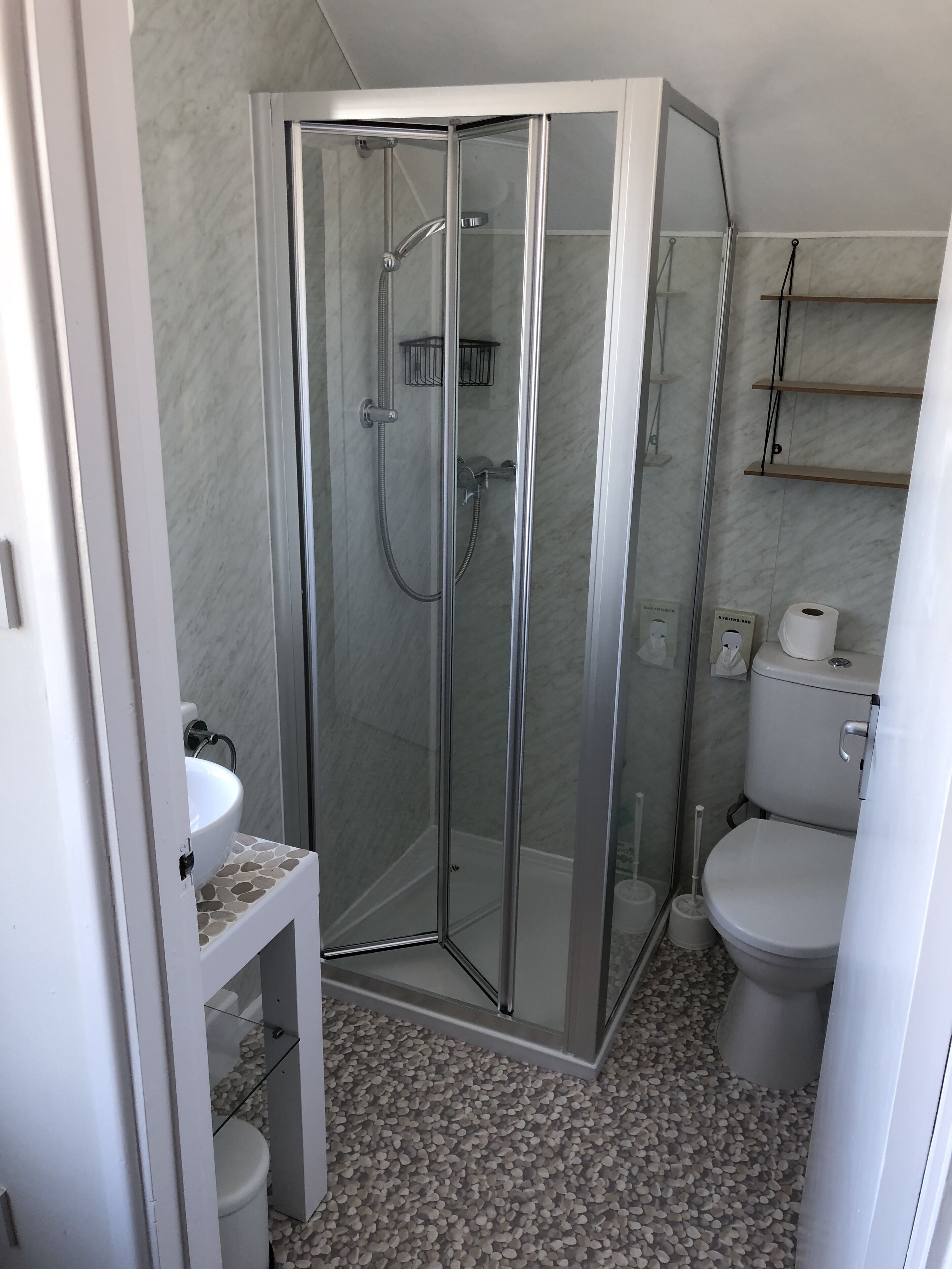 Een moderne badkamer met een glazen douchecabine, een wit toilet en een vloer van marmer.