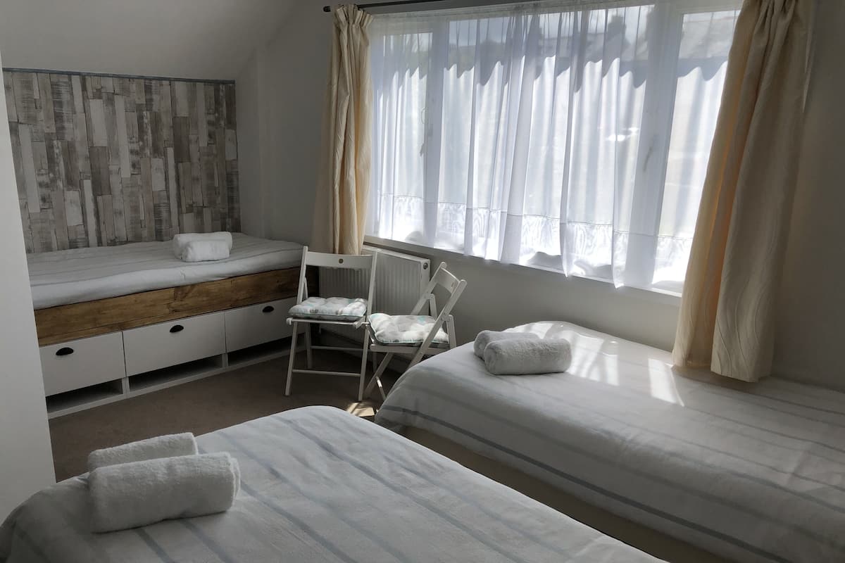 Ett sovrum med två sängar, en stol, ett litet skrivbord och ett fönster med gardiner.