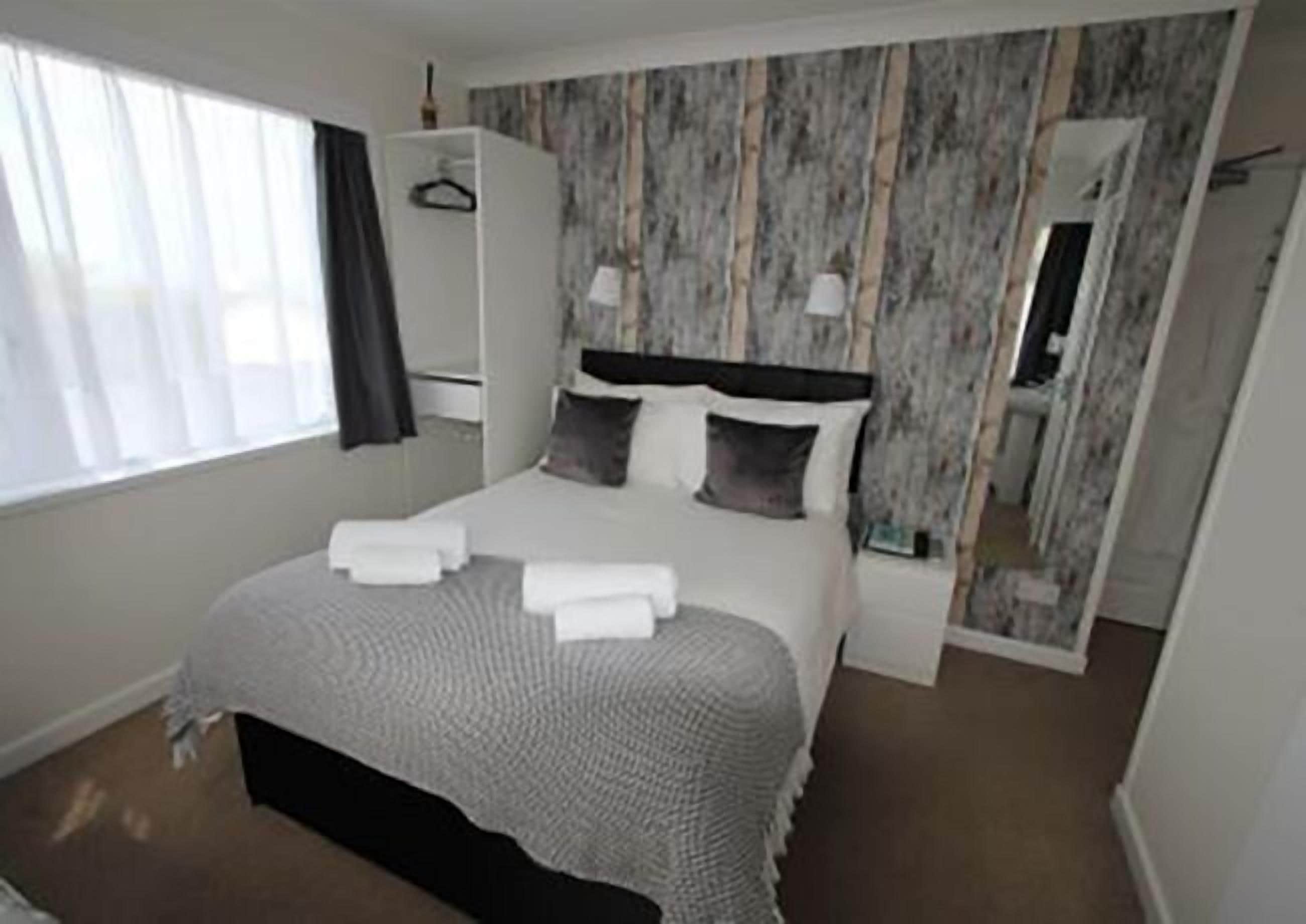 A hotel room with a bed, a wardrobe, a mirror, and a window.