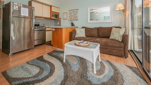 A compact living space with a kitchenette, a brown sofa, a small white table, and a ceiling fan.