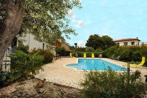 Una piscina con solárium de piedra, rodeada de follaje y un árbol.