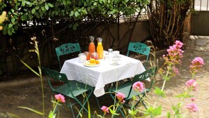 A table set outdoors with a white tablecloth, surrounded by green chairs, and various breakfast items including juice and eggs. - L'escalivade Chambres d'hôtes (Ceret)