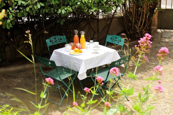 A table set outdoors with a white tablecloth, surrounded by green chairs, and various breakfast items including juice and eggs. - L'escalivade Chambres d'hôtes (Ceret)