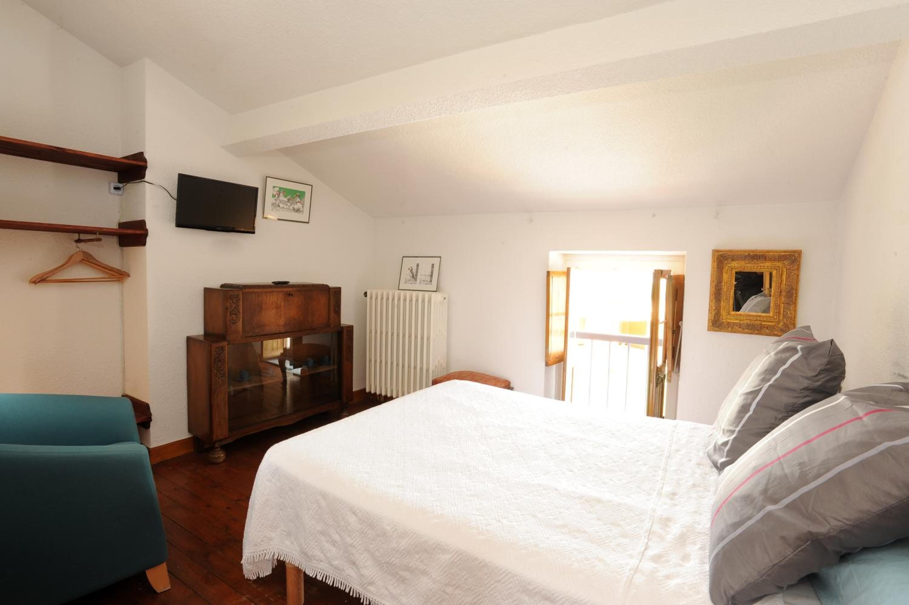 Een slaapkamer met een bed, een dressoir, een televisie en een radiator.