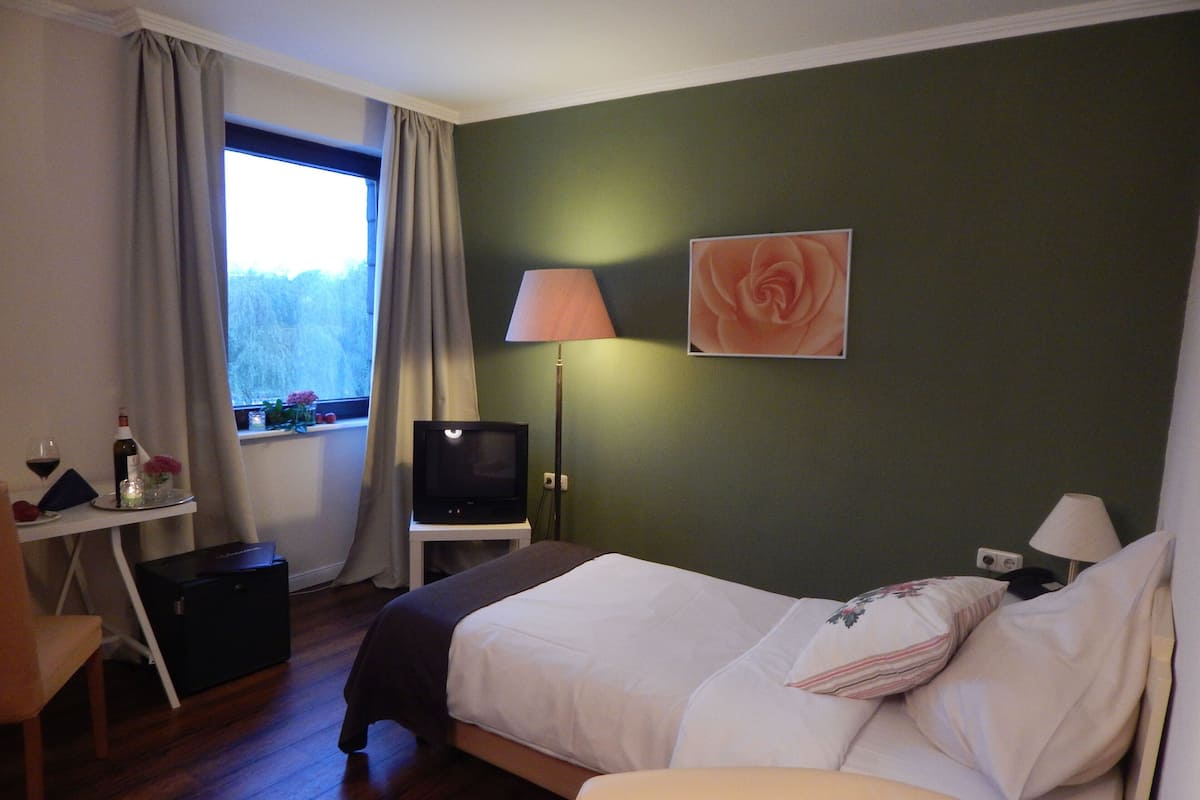 A hotel room with a bed, a desk with a television, a lamp, and a window with curtains.