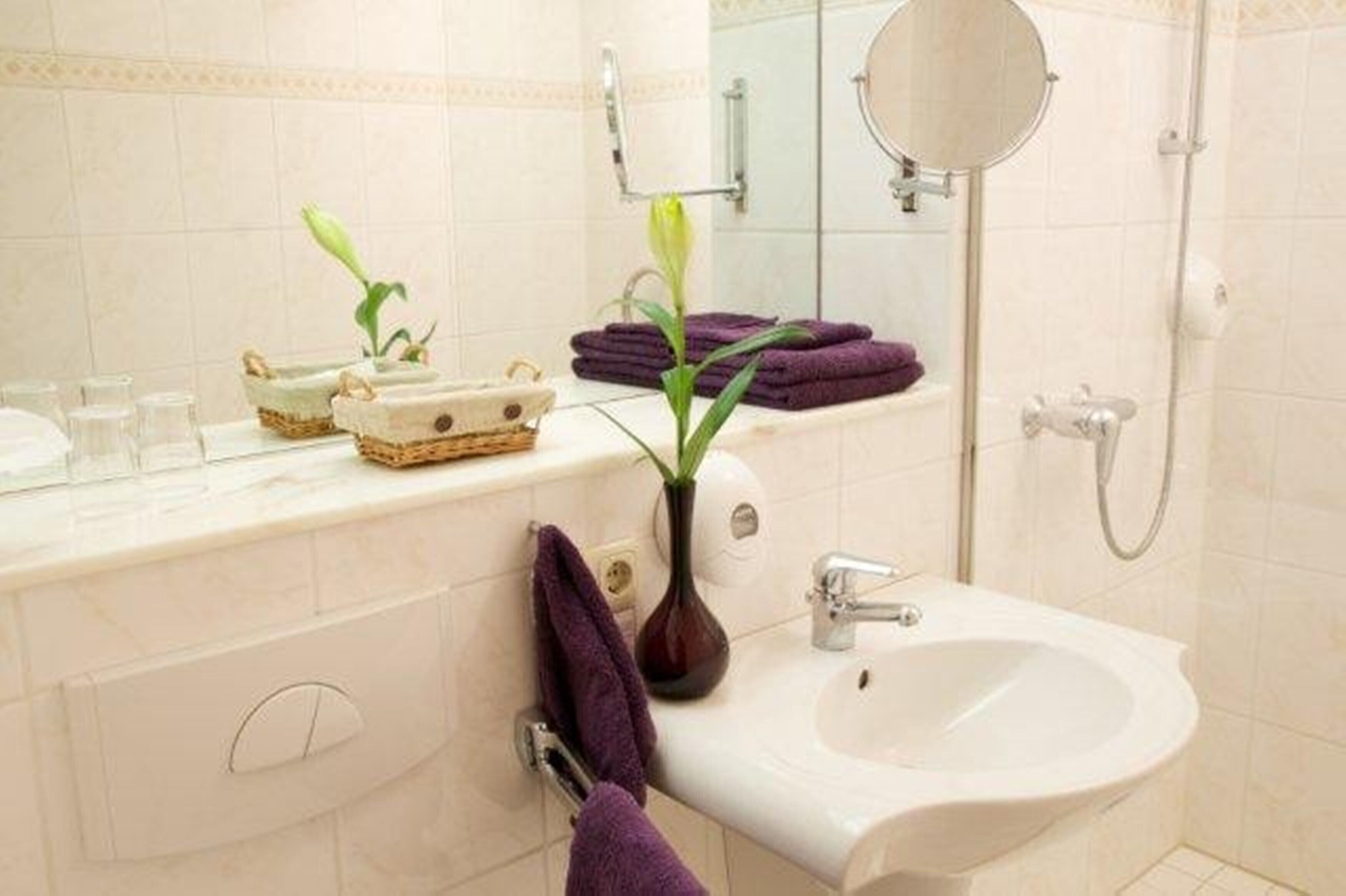 A bathroom with a white sink, a mirror, a towel rack, and a vase with a plant.