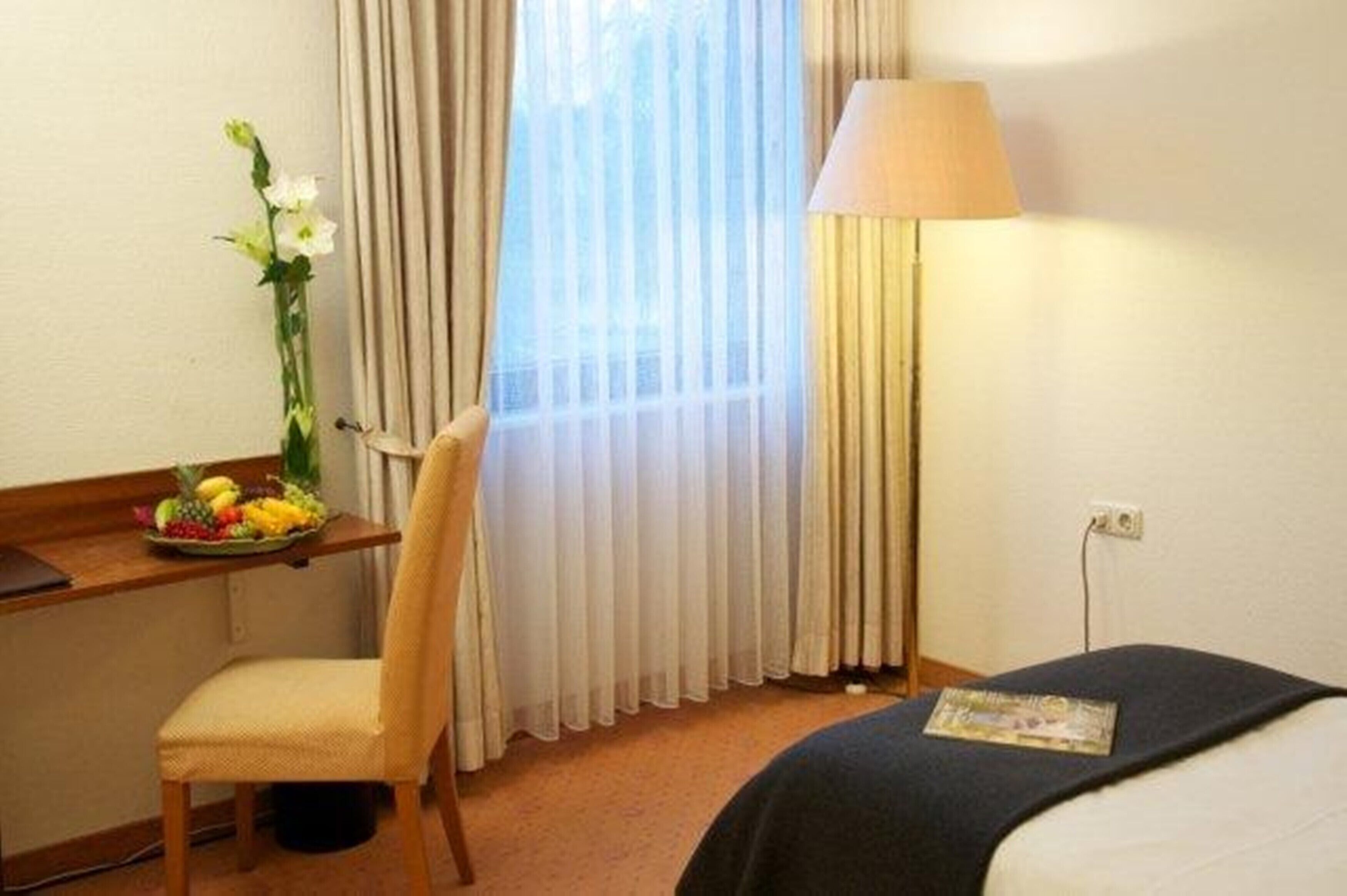A hotel room with a bed, a desk with a lamp, a chair, and a fruit basket.